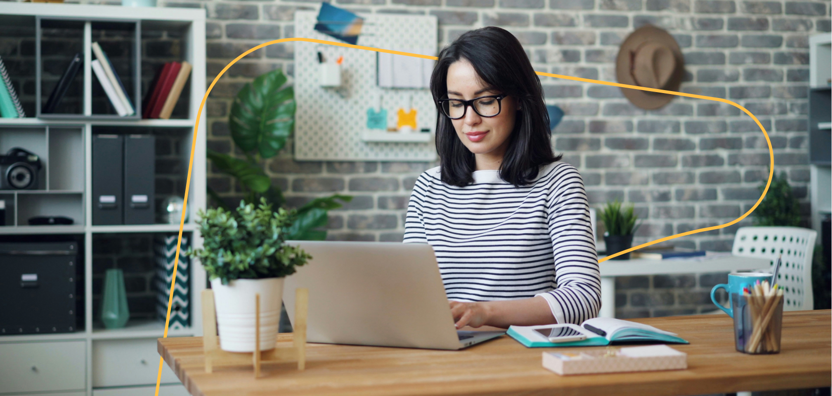 Small business owner in glasses working on a laptop at a wooden desk in a bright home office